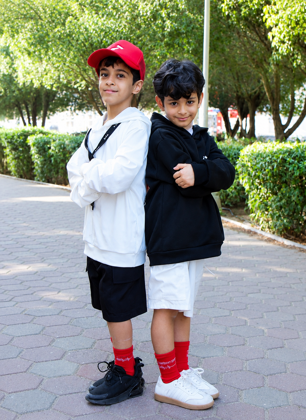 Two boys in JADDAH hoodies and red socks standing back to back on a paved park walkway.