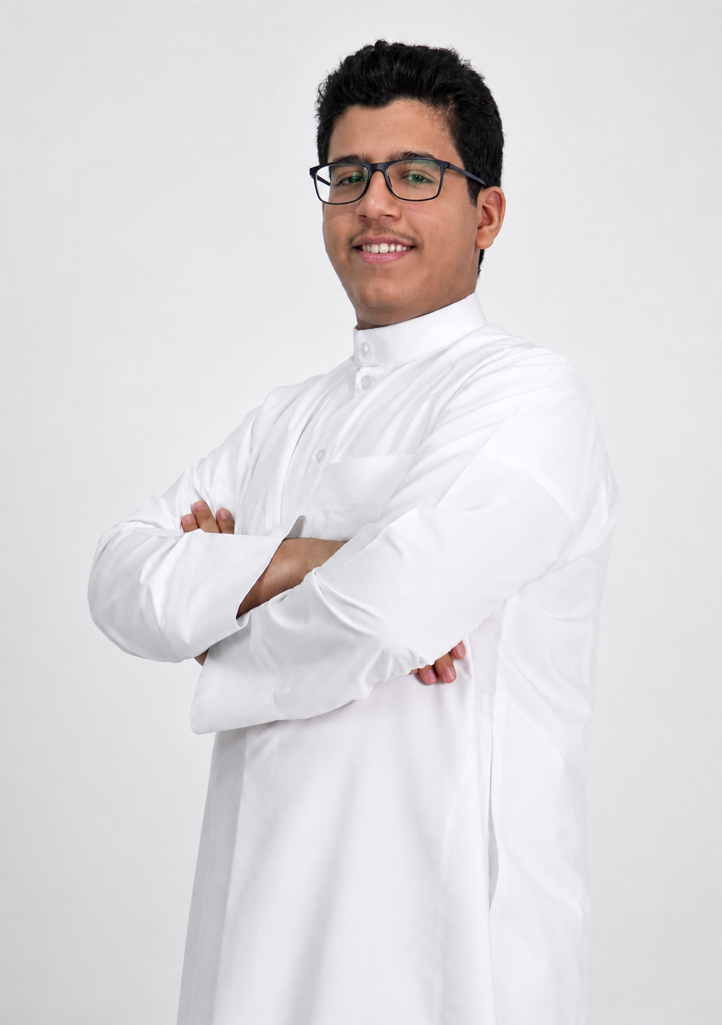 Youssef Rami wearing glasses and a white thobe, arms crossed, against a light grey studio backdrop.